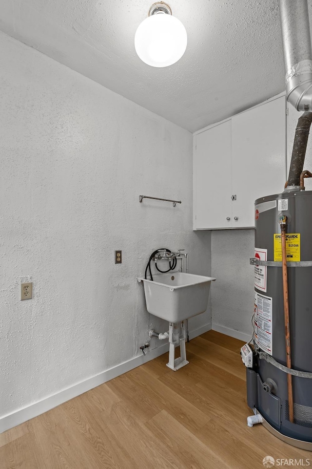 washroom featuring strapped water heater, cabinet space, baseboards, and wood finished floors