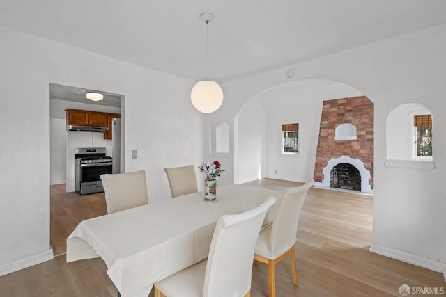 dining area with light wood finished floors, a stone fireplace, arched walkways, and baseboards