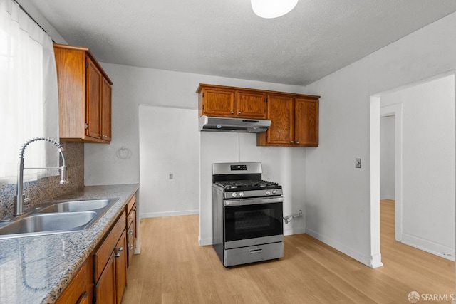 kitchen with stainless steel gas range oven, under cabinet range hood, a sink, brown cabinetry, and light wood finished floors