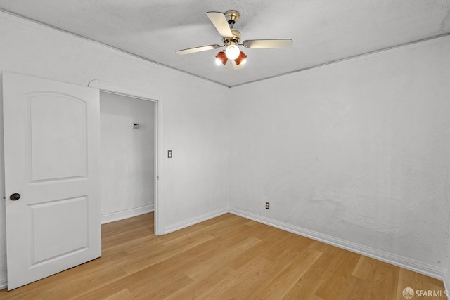 empty room with a textured ceiling, a ceiling fan, light wood-type flooring, and baseboards