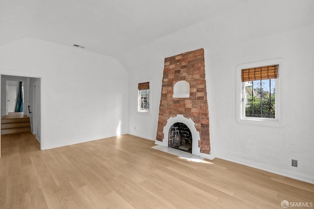 unfurnished living room with lofted ceiling, light wood-style flooring, a fireplace, and visible vents