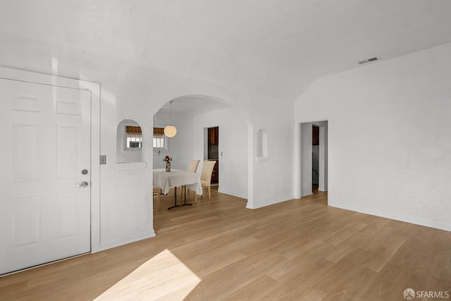 entrance foyer with arched walkways, visible vents, light wood-type flooring, and lofted ceiling