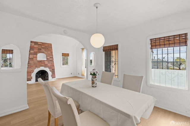 dining room featuring a large fireplace, baseboards, arched walkways, and light wood-style flooring