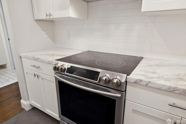 kitchen featuring light stone countertops, decorative backsplash, electric stove, and white cabinets