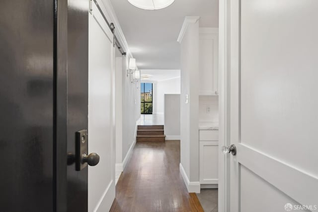 hallway featuring a barn door, ornamental molding, and dark hardwood / wood-style flooring