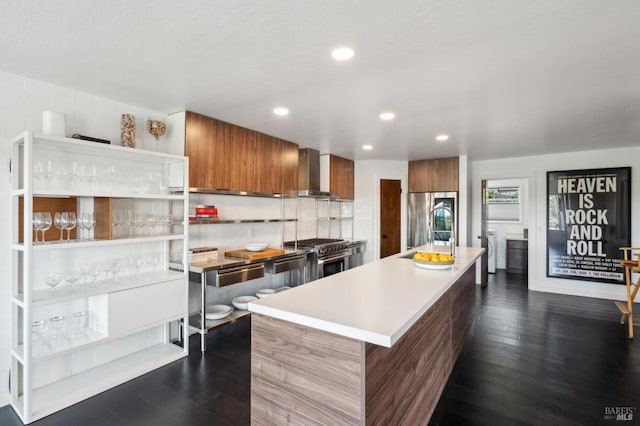 kitchen featuring wall chimney exhaust hood, modern cabinets, stainless steel appliances, brown cabinets, and dark wood-style floors