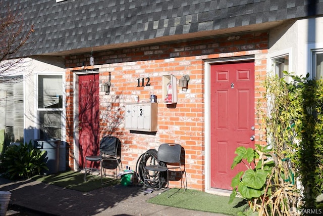 property entrance with mansard roof, roof with shingles, and brick siding