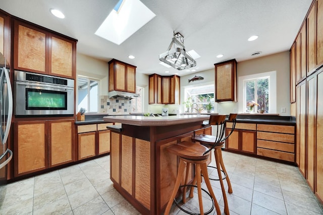 kitchen featuring recessed lighting, a kitchen breakfast bar, a skylight, brown cabinetry, and stainless steel oven