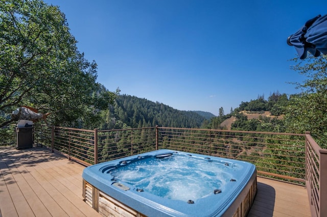 deck featuring a view of trees and hot tub deck surround