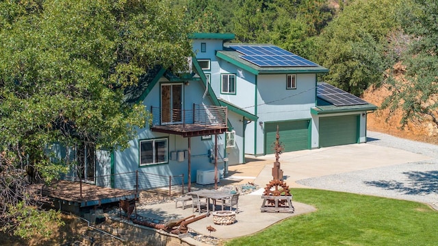 view of front of property with concrete driveway, a patio area, a balcony, roof mounted solar panels, and an outdoor fire pit