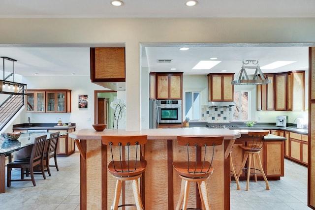 kitchen featuring a skylight, brown cabinetry, a kitchen bar, appliances with stainless steel finishes, and a kitchen island