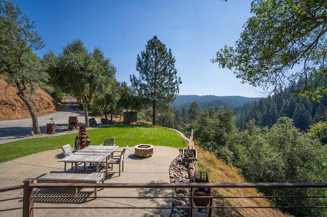 surrounding community featuring a fire pit, a patio area, a lawn, and a wooded view