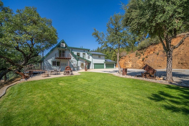 rear view of house featuring a lawn, driveway, an outdoor fire pit, an attached garage, and a patio