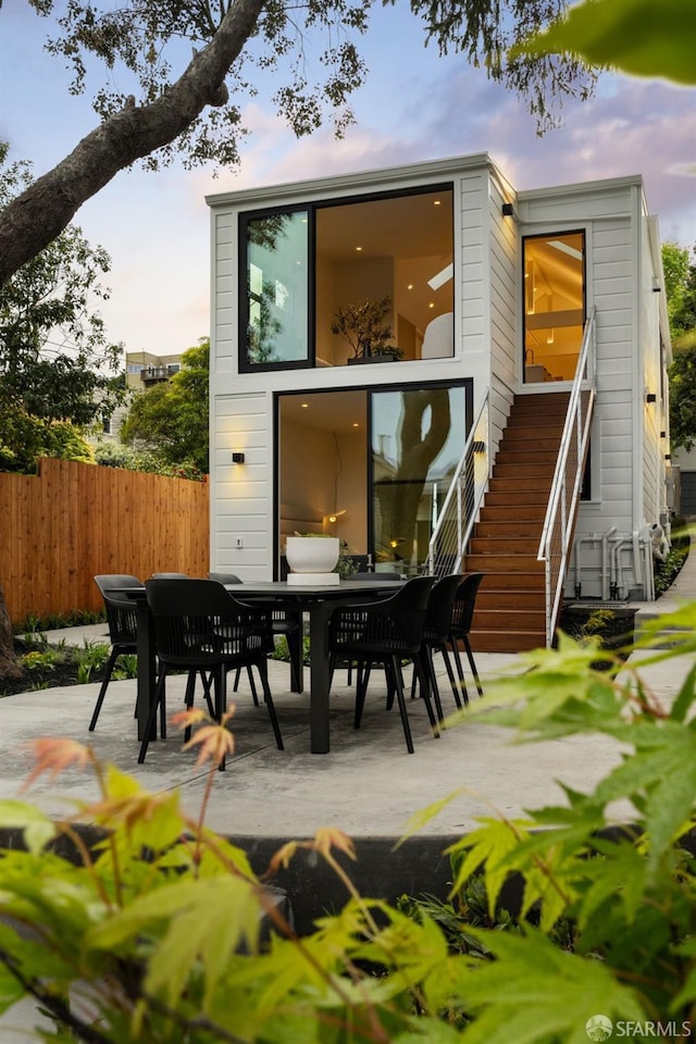 rear view of house featuring stairs, a patio area, fence, and outdoor dining space