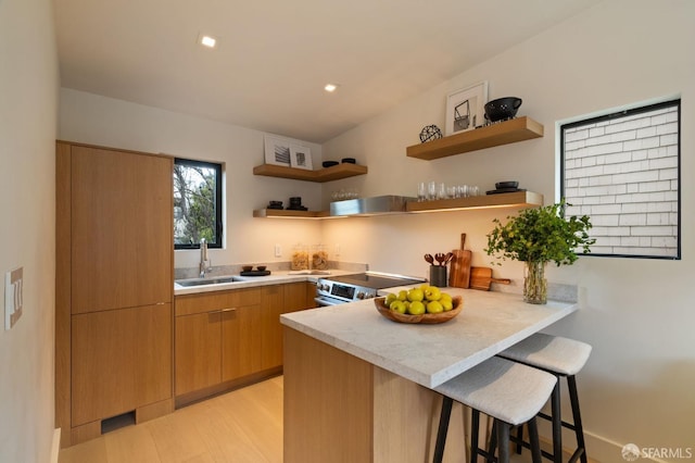 kitchen featuring a kitchen breakfast bar, stainless steel electric range oven, open shelves, a sink, and a peninsula