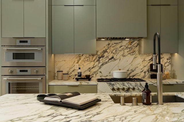 kitchen featuring stainless steel double oven, decorative backsplash, light stone counters, and modern cabinets