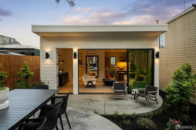 back of house at dusk featuring fence and a patio