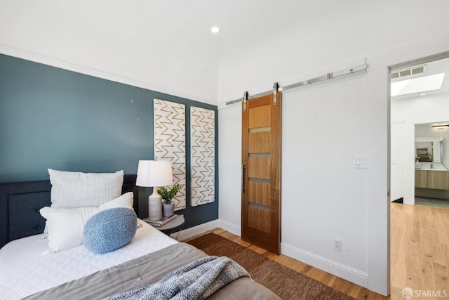 bedroom featuring a barn door, baseboards, visible vents, and wood finished floors