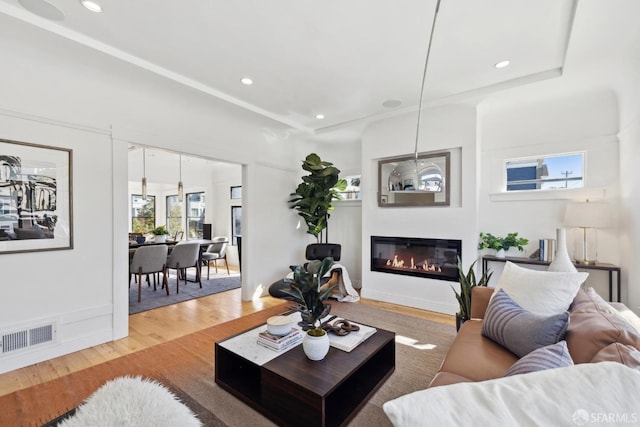 living area with visible vents, recessed lighting, a glass covered fireplace, and wood finished floors