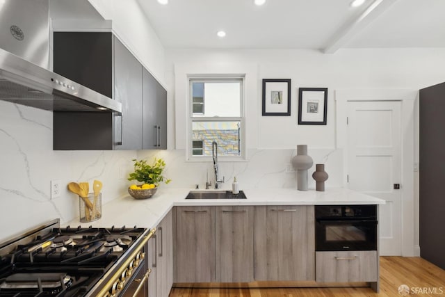 kitchen featuring black oven, wall chimney range hood, gas range, modern cabinets, and a sink