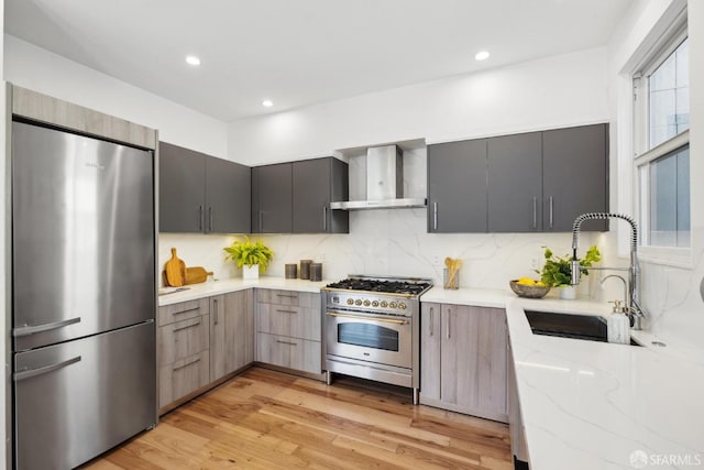 kitchen with modern cabinets, stainless steel appliances, wall chimney exhaust hood, and light stone countertops