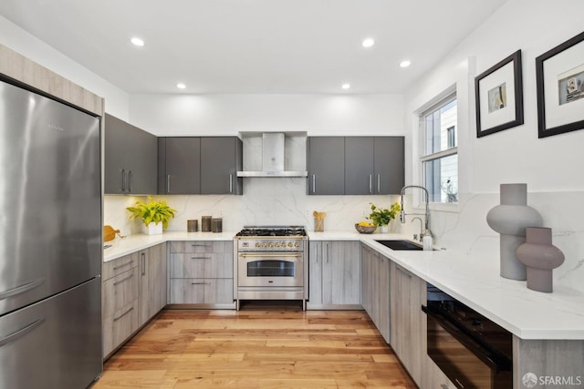 kitchen with gray cabinetry, a sink, appliances with stainless steel finishes, wall chimney exhaust hood, and modern cabinets