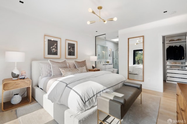 bedroom with a walk in closet, a notable chandelier, and light hardwood / wood-style floors