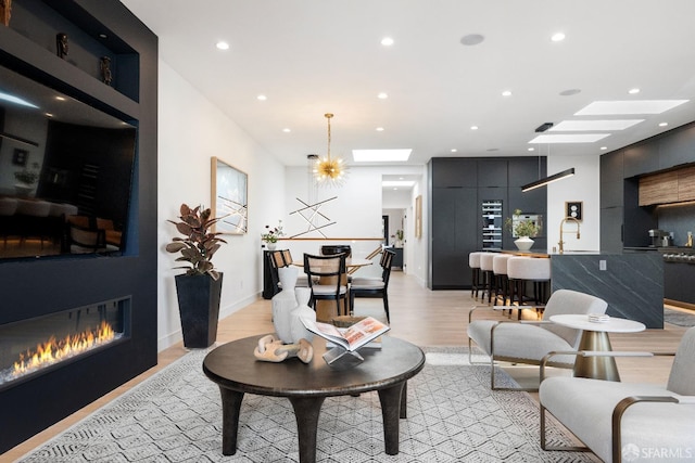 living room with a notable chandelier, light wood-type flooring, and a skylight