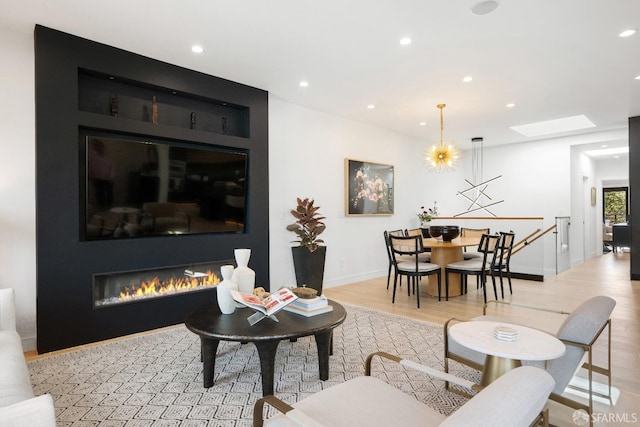 living room with an inviting chandelier, a skylight, and light hardwood / wood-style flooring