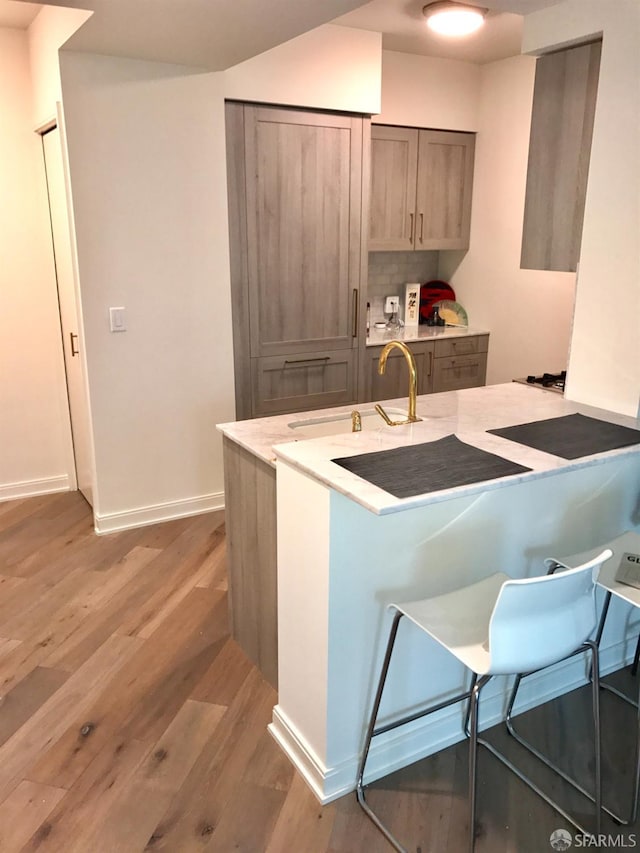 kitchen with light countertops, backsplash, a sink, light wood-type flooring, and baseboards