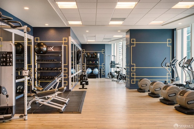 gym with a wall of windows, a drop ceiling, and wood finished floors