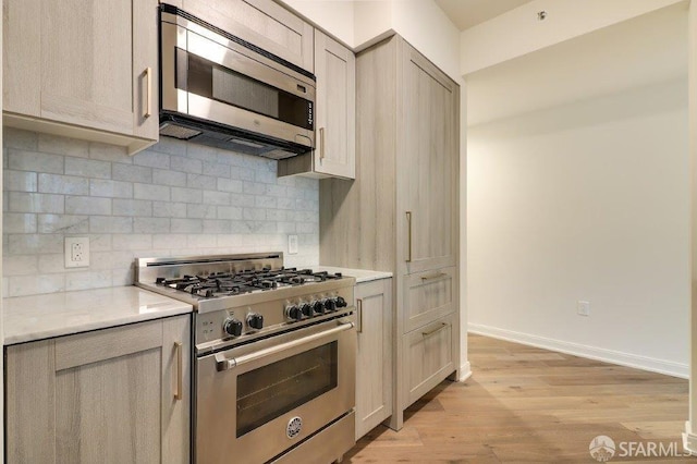 kitchen featuring light wood-style floors, stainless steel appliances, baseboards, and tasteful backsplash