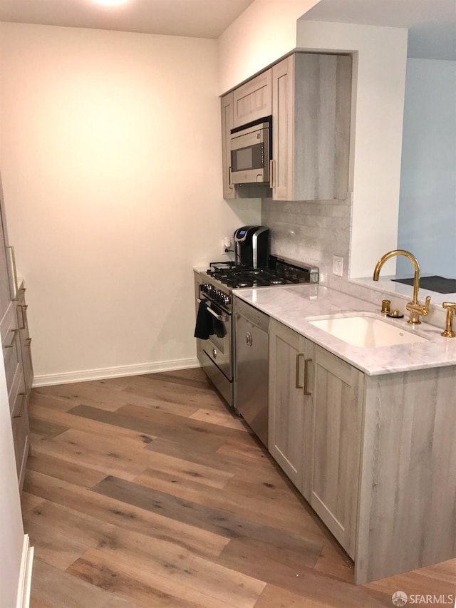 kitchen with tasteful backsplash, appliances with stainless steel finishes, a peninsula, light wood-style floors, and a sink