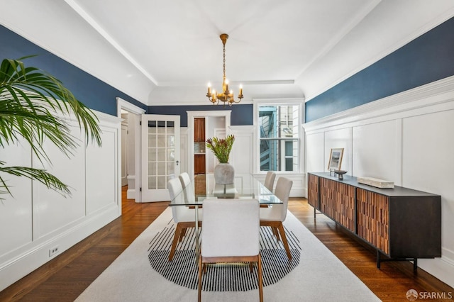 dining room featuring dark wood finished floors, a decorative wall, a chandelier, and wainscoting