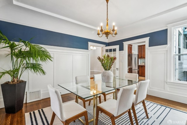 dining area with visible vents, a decorative wall, wood finished floors, and a chandelier