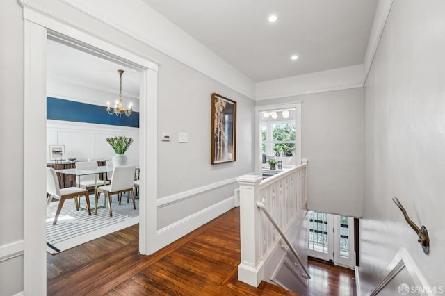 hall with a decorative wall, dark wood-style floors, recessed lighting, a notable chandelier, and an upstairs landing