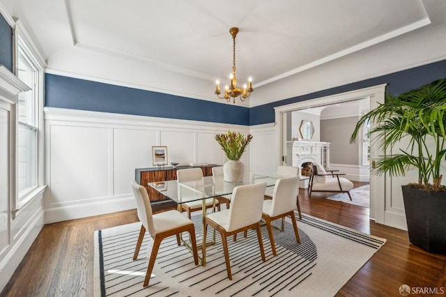 dining room featuring wood finished floors, a raised ceiling, a notable chandelier, a decorative wall, and a wealth of natural light