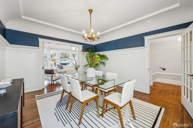 dining area with wainscoting, a decorative wall, dark wood finished floors, and a notable chandelier