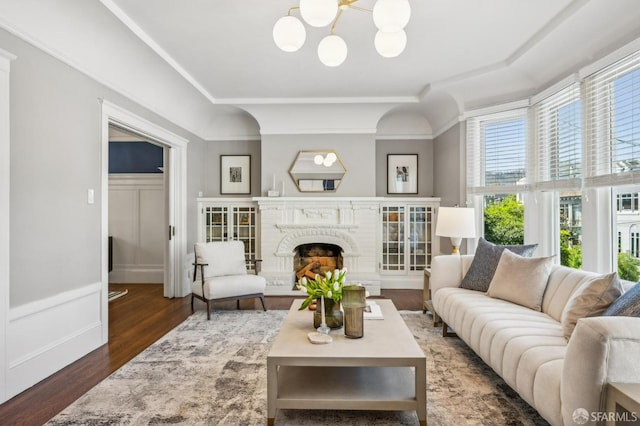 living room with a brick fireplace, an inviting chandelier, wood finished floors, and a decorative wall