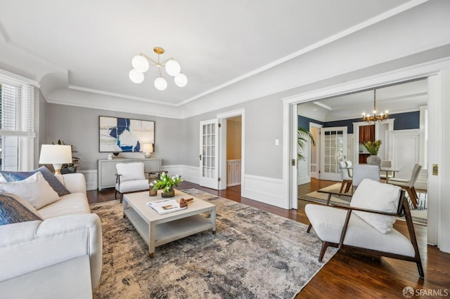 living room with crown molding, wainscoting, wood finished floors, an inviting chandelier, and a tray ceiling