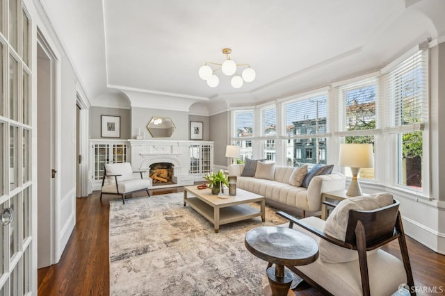 living room featuring dark wood-type flooring, a raised ceiling, a chandelier, and a fireplace