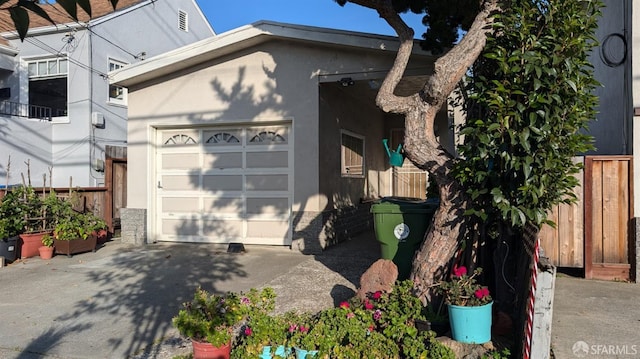 view of side of home featuring fence, driveway, stucco siding, and a garage
