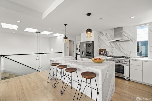 kitchen with wall chimney exhaust hood, stainless steel appliances, white cabinets, and an island with sink