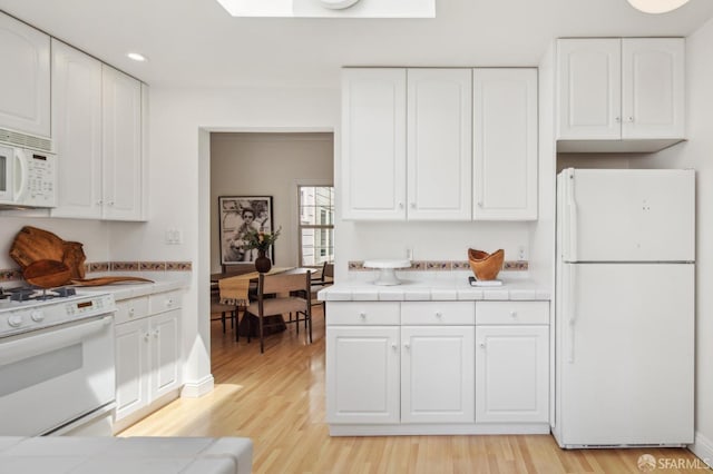 kitchen with light wood-style floors, white cabinets, tile countertops, and white appliances