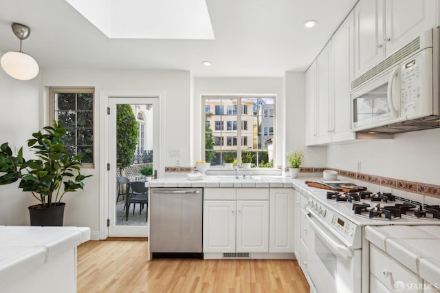 kitchen with tile counters, light wood finished floors, and white appliances