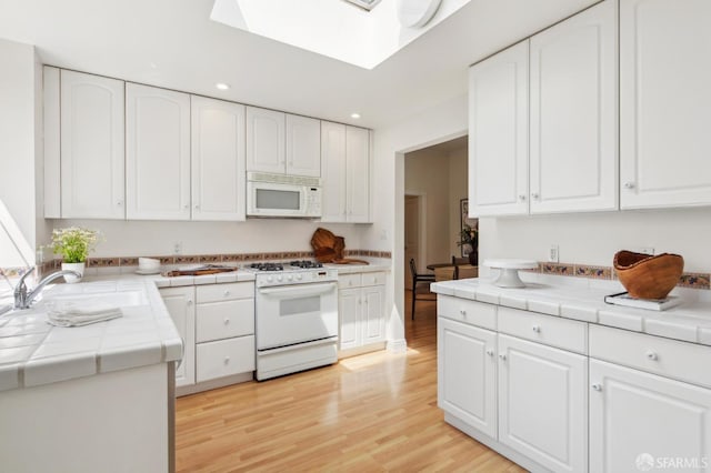 kitchen featuring a skylight, a sink, tile counters, recessed lighting, and white appliances