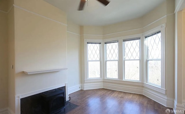 unfurnished living room with dark hardwood / wood-style flooring, a wood stove, ceiling fan, and a healthy amount of sunlight