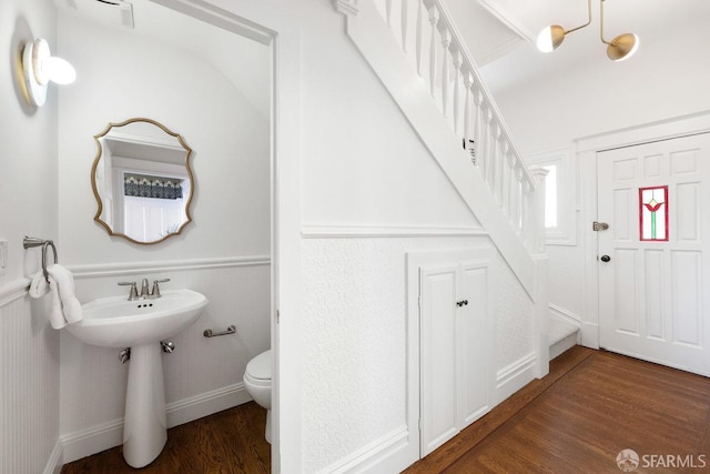 half bath with a wainscoted wall, wood finished floors, and toilet