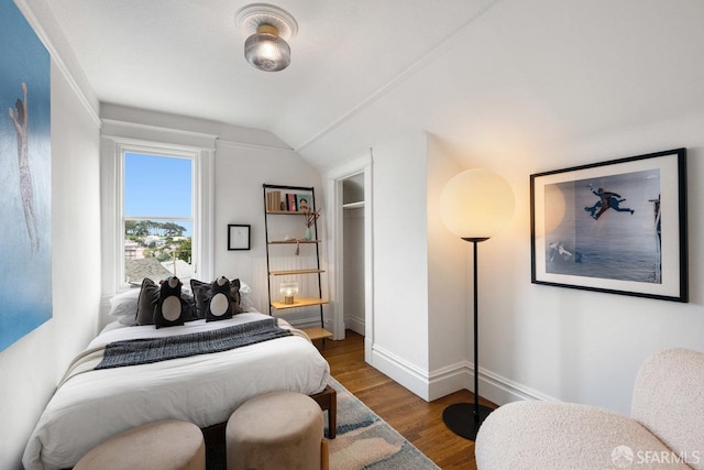 bedroom with vaulted ceiling, wood finished floors, and baseboards