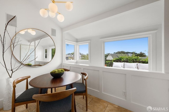 dining space with a notable chandelier, a wainscoted wall, a decorative wall, visible vents, and vaulted ceiling